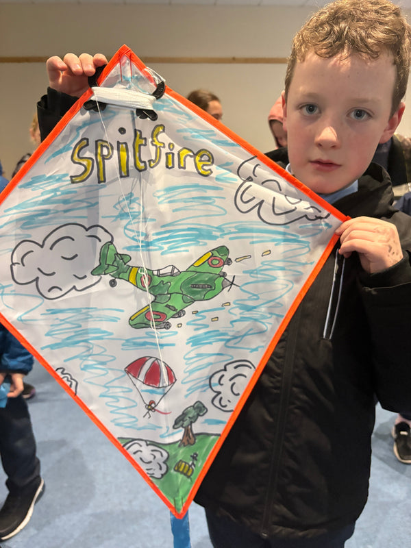 child holding kite with spitfire flying in sky